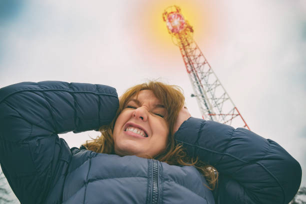The woman is holding her head near the BTS. Harmful radiation from cellular network transmitters concept