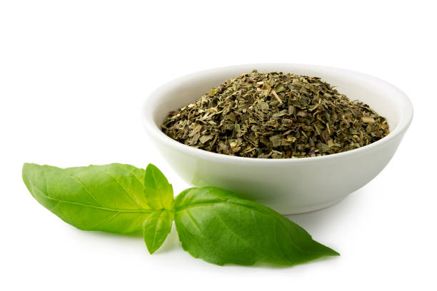 istock Dried chopped basil in white ceramic bowl next to fresh basil leaves isolated on white. 1126473867