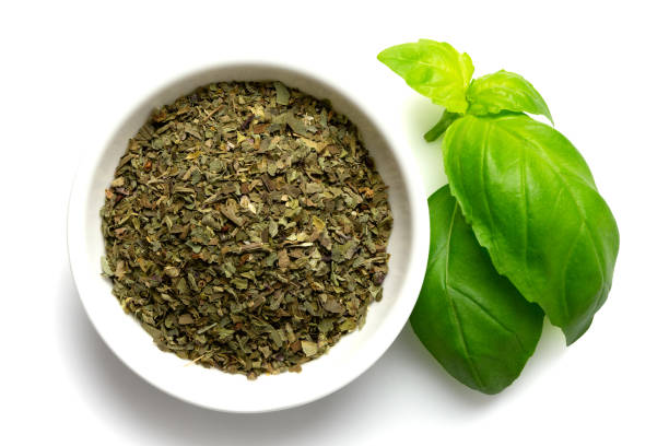 istock Dried chopped basil in white ceramic bowl next to fresh basil leaves isolated on white from above. 1126474046