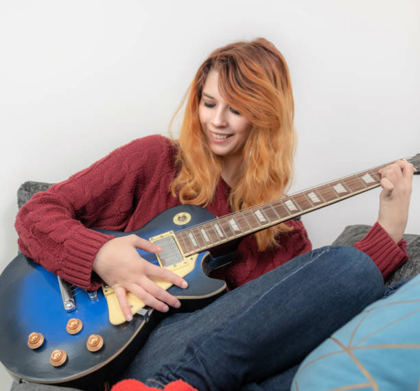 istock Young woman practising the guitar on the sofa 1126477261