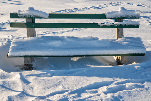 Wooden bench covered with snow in a park waits for companionship.