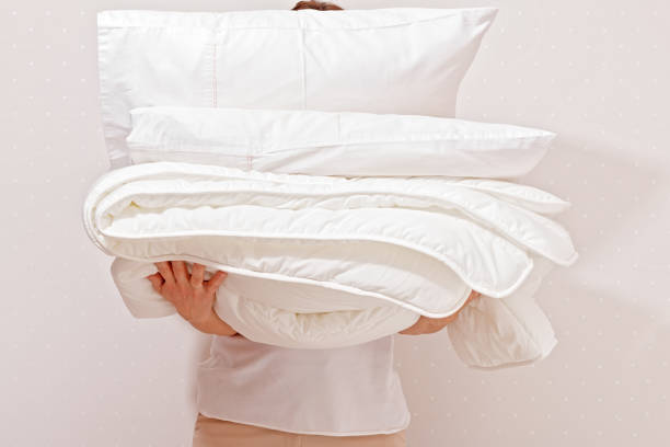 睡眠のための寝具の山を保持している女性。世帯 - シーツ ストックフォトと画像