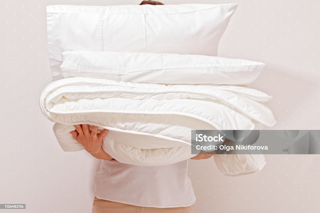 Woman holding a pile of bedding for sleeping. Household Duvet Stock Photo