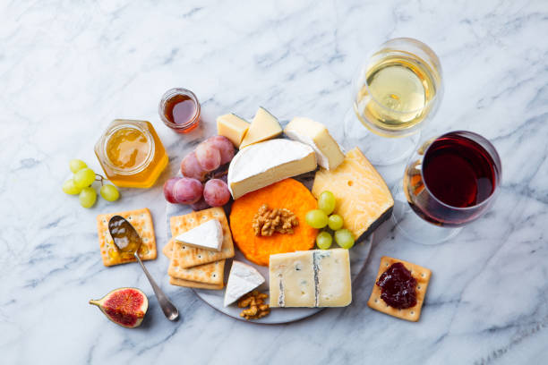 assortiment de fromages, raisin rouge et blanc vin dans des verres. fond de marbre. vue de dessus. - cheese portion cracker cheddar photos et images de collection
