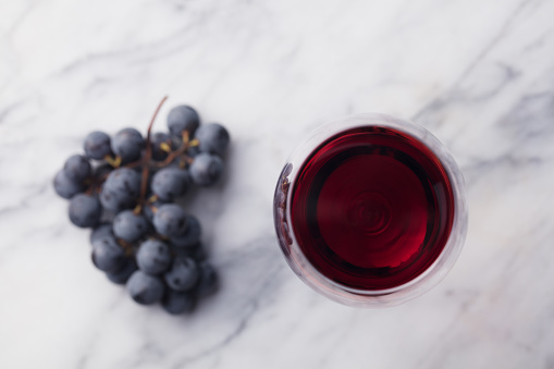 Red wine in glass with fresh grape on marble table background. Top view