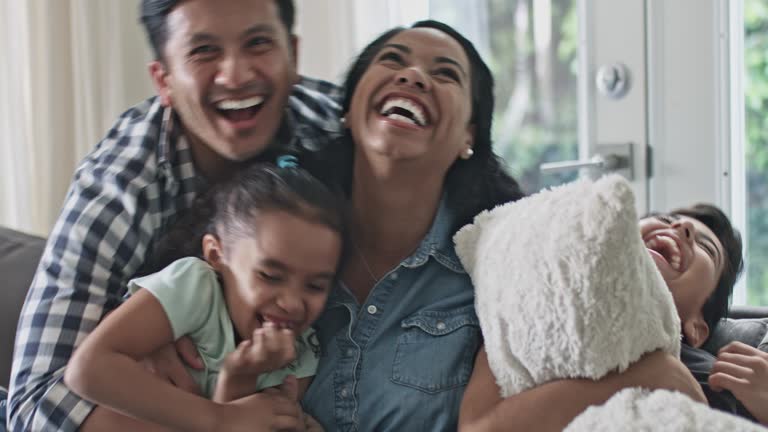Portrait of smiling multi-ethnic family. Father joins in the sofa with the family and start tickling everybody.