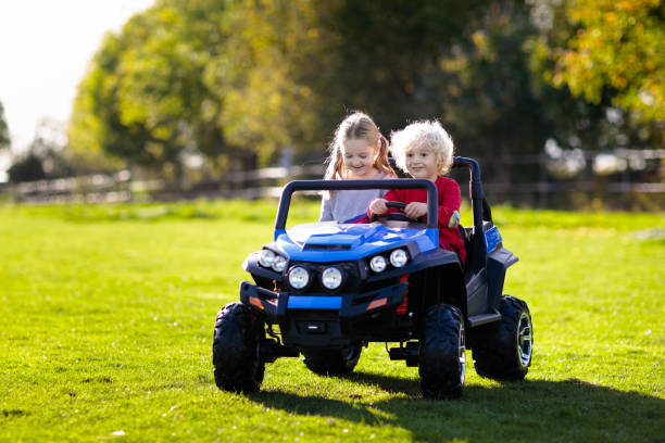 Kids driving electric toy car. Outdoor toys. Kids driving electric toy car in summer park. Outdoor toys. Children in battery power vehicle. Little boy and girl riding toy truck in the garden. Family playing in the backyard. toy vehicle stock pictures, royalty-free photos & images