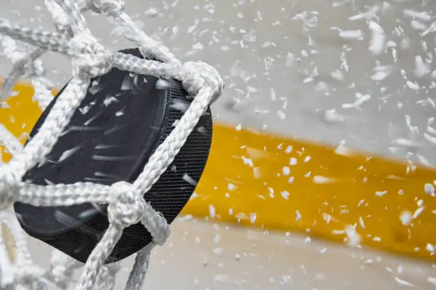 Photo of Close-up of an Ice Hockey puck hitting the back of the net as snow flies, side view