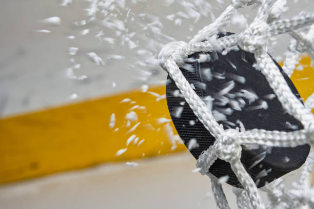 close-up of an ice hockey puck hitting the back of the net as snow flies, side view - ice hockey hockey puck playing shooting at goal imagens e fotografias de stock