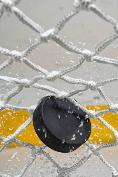 close-up of an ice hockey puck hitting the back of the net as snow flies, front view - ice hockey hockey puck playing shooting at goal imagens e fotografias de stock