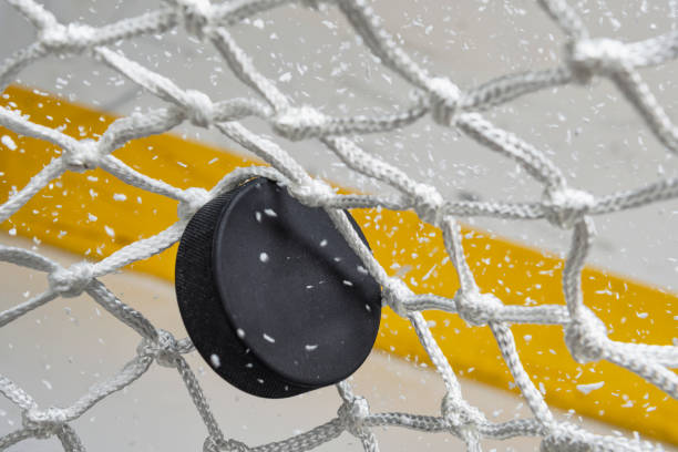 primo piano di un disco da hockey su ghiaccio che colpisce la parte posteriore della rete mentre la neve vola, vista frontale - hockey foto e immagini stock