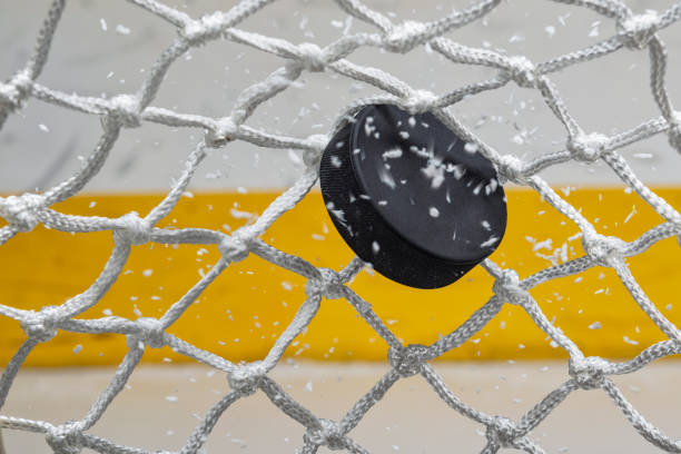 close-up of an ice hockey puck hitting the back of the net as snow flies, front view - ice hockey hockey puck playing shooting at goal imagens e fotografias de stock