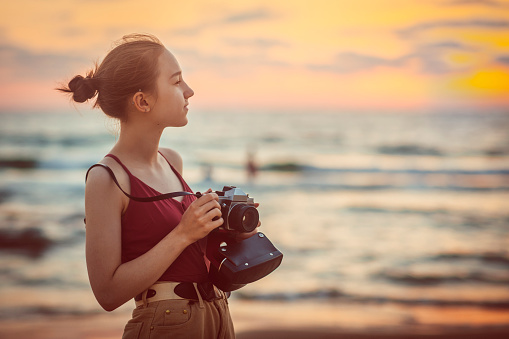 Young photographer taking a photo on the beach with a film camera, sunset