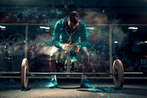 Attractive Caucasian man in sweatshirt and shorts preparing to lift barbells. Chalk all around, in background mirror. Attractive Caucasian man in sweatshirt and shorts preparing to lift barbells. Chalk all around, in background mirror. sports chalk stock pictures, royalty-free photos & images