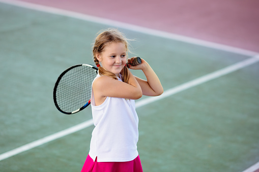 Child playing tennis on indoor court. Little girl with tennis racket and ball in sport club. Active exercise for kids. Summer activities for children. Training for young kid. Child learning to play.