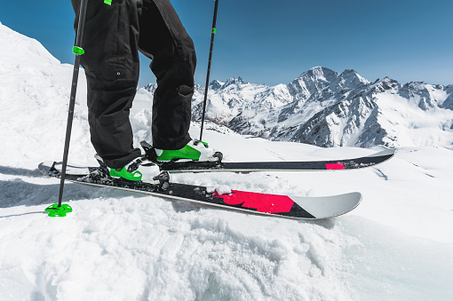 A close-up of the ski on the athlete's feet against the background of snow-capped rocky mountains. The concept of winter sports in the mountains.
