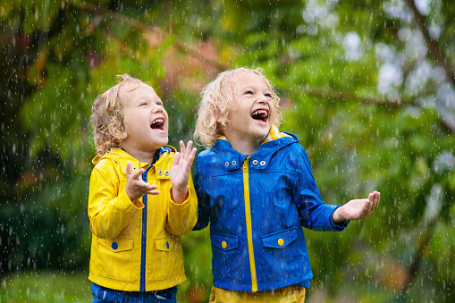 Kids play in autumn rain. Child playing outdoor on rainy day. Little boy catching rain drops under heavy shower. Fall storm in a park. Waterproof wear for kid. Children outdoors by any weather.