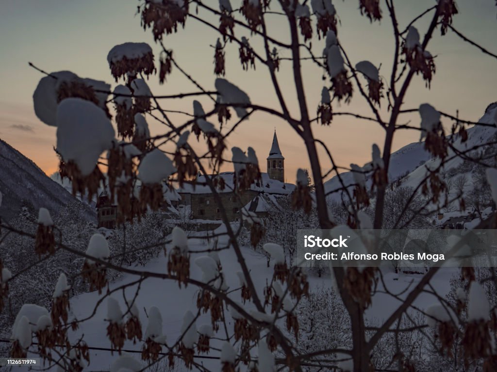 Unha sunset covered by snow Sunset over a mountain village at winter behid a tree Beauty In Nature Stock Photo