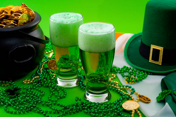 das glück der irischen meme und glücklich st patricks day konzept thema mit zwei gläsern aus gefärbten bier, kobold hut, perlen halskette und topf mit gold-münzen auf der irland-flagge auf grünem hintergrund isoliert - green beer fotos stock-fotos und bilder