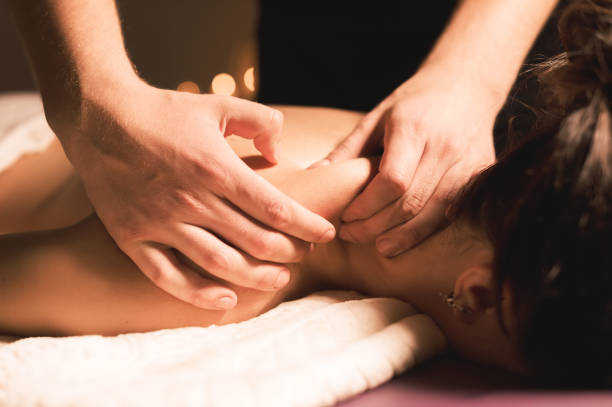 mains d’hommes faire un cou thérapeutique de massage pour une fille couché sur un divan de massage dans un spa de massage avec éclairage sombre. gros plan. touche noire - massaging massage therapist rear view human hand photos et images de collection