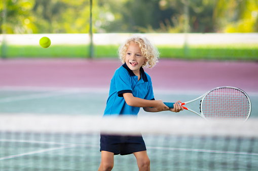 Child playing tennis on indoor court. Little boy with tennis racket and ball in sport club. Active exercise for kids. Summer activities for children. Training for young kid. Child learning to play.
