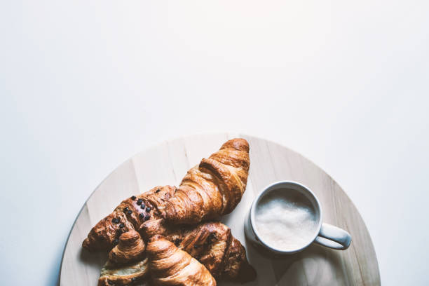 Bunch of croissants and cup of cappuccino on wooden disk. View from top on white background.