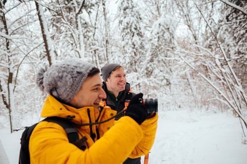Smiling hikers walking through the snowy forest and capturing nature