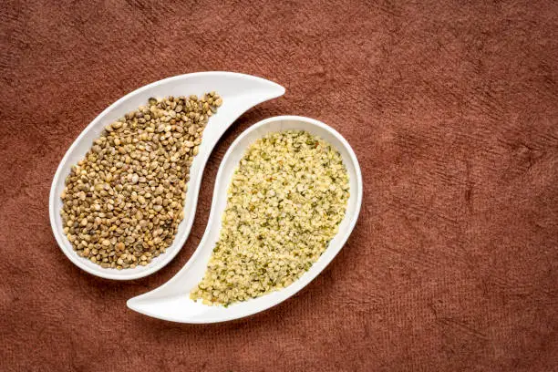 dry hemp seeds and hearts in small teardrop bowls against brown textured paper