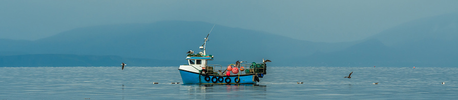 Small Fishing Boat With Lobster Pods And Seagulls On Calm Atlantic In Front Of The Hebride Islands