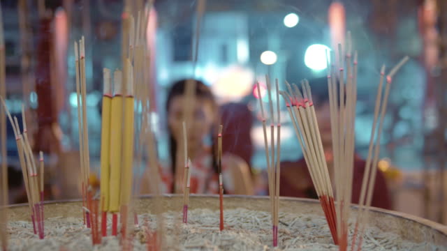 Chinese couple holding light incense stick and candle to pay respect in temple.