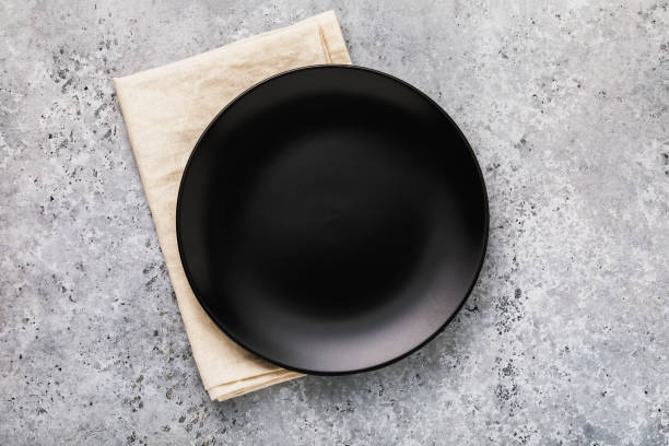 Empty ceramic plate in black with a napkin on a gray concrete table, top view stock photo