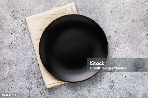 Empty Ceramic Plate In Black With A Napkin On A Gray Concrete Table Top View Stock Photo - Download Image Now