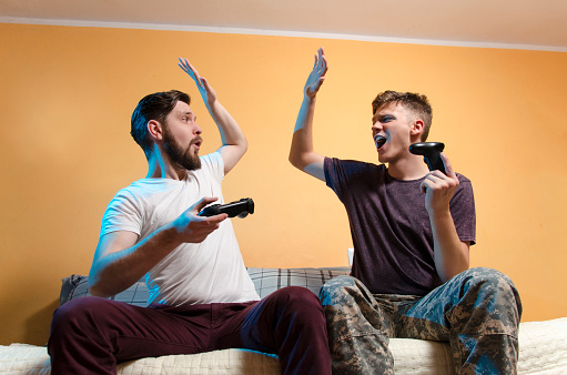 Young adult man and teenager giving high five to each other while playing video games