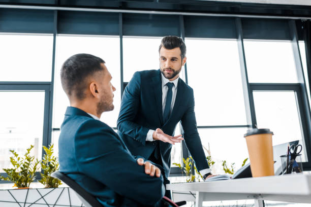istock handsome businessman looking at coworker while talking in modern office 1126564440