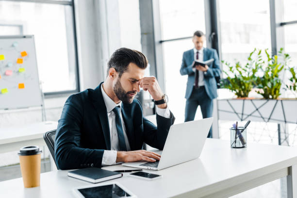 istock selective focus of tired businessman holding head in modern office 1126564502