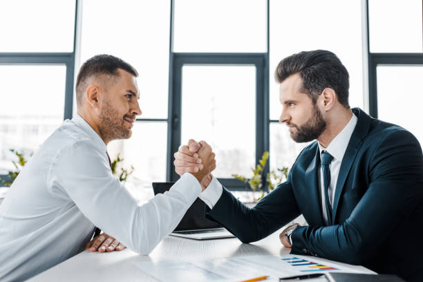 empresarios guapos compitiendo vencidas en oficina moderna - conflict competition arm wrestling business fotografías e imágenes de stock