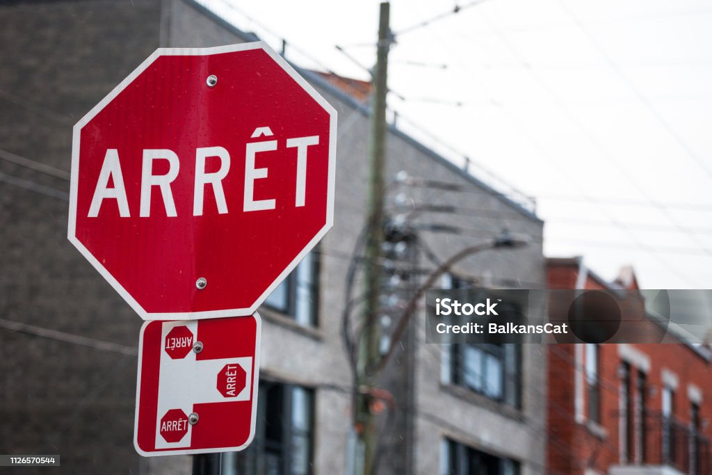 Quebec Stop Sign, obeying by bilingual rules of the province imposing the use of French language on roadsigns, thus translated Stop into Arret, taken in the streets of Montreal, Canada Picture of a Quebec stop sign, translated in French, called according to Quebec French speaking regulations panneau d'arret Sign Stock Photo