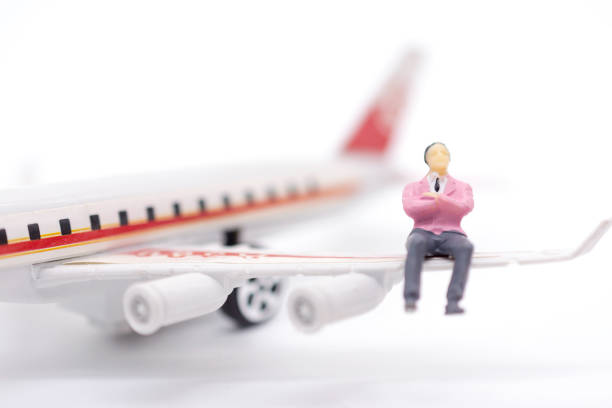 istock Miniature businessman sitting on airplane wing on white background 1126573525