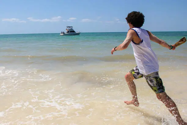 A happy young guy is running along the water by the sea, enjoying his vacation.