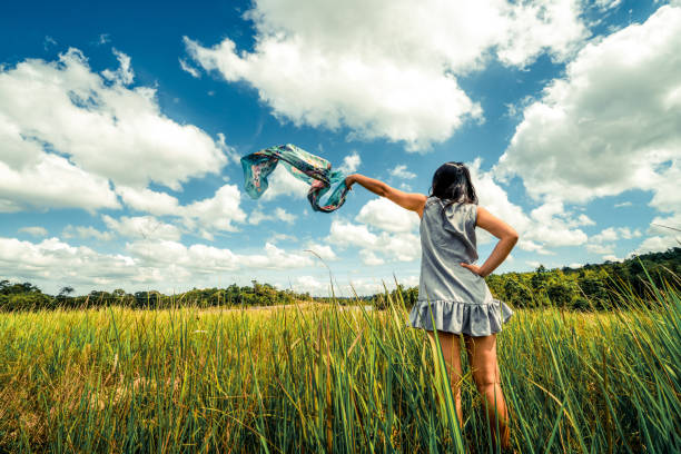 Young beautiful woman on green grass meadow spreading arms to the blue sunny sky on summer day. Getaway and meditation concept.