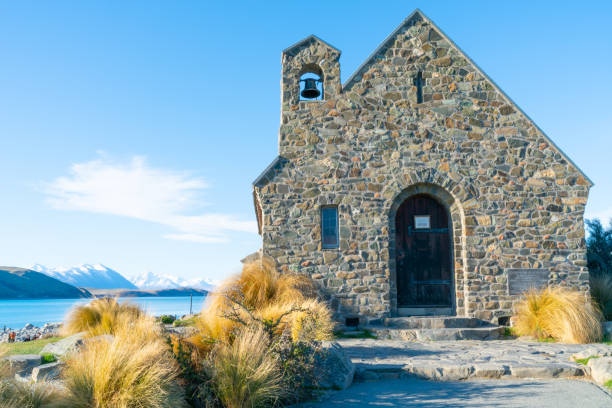 iconic small stone church Church of Good Shepherd against background aqua lake and scenic snow capped Southern Alps  October 2018 at Lake Pukaki New Zealand