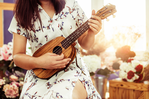 Happy woman musician playing ukulele and singing a song in sound studio. Music lifestyle concept.