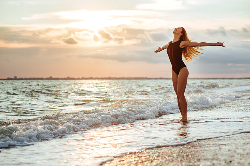 Outdoor lifestyle portrait of beautiful girl in black swimsuit. Young hipster woman play with her hair. She is happy. Sunny hot summer day at tropical ocean beach.