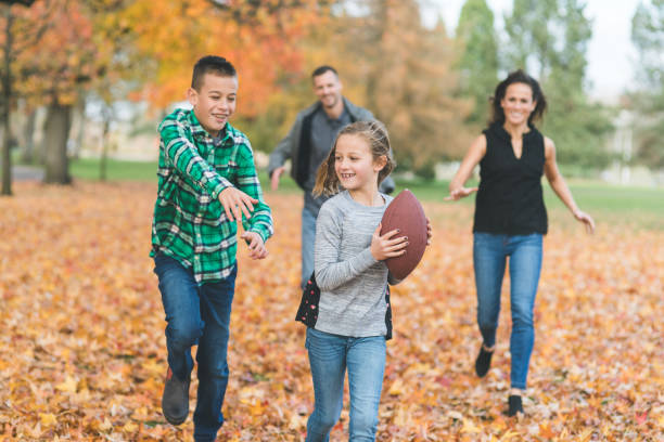 famiglia che gioca a calcio insieme nelle foglie autunnali - football player group of people running american football foto e immagini stock