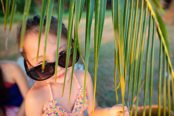 Adorable little girl in floral summer dress and orange sunglasses enjoying a sunny day at the beach