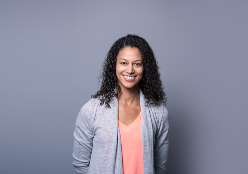 Portrait of mid adult businesswoman smiling. Beautiful female professional is standing against gray background. She is wearing smart casuals.