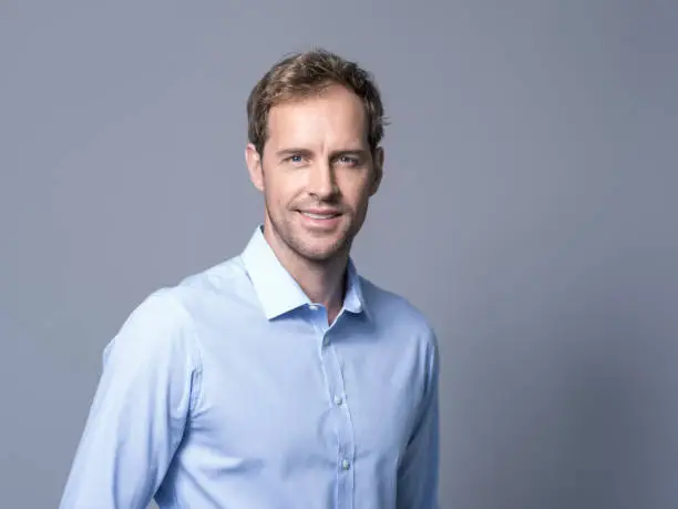 Portrait of businessman smiling over gray background. Confident mid adult executive is wearing shirt. Handsome male is with blue eyes.