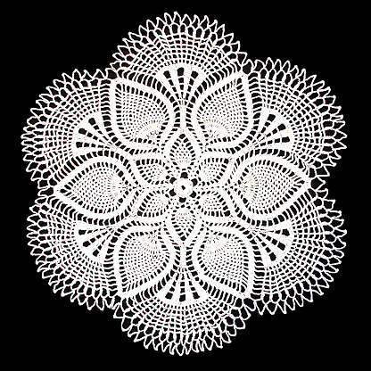 Isolated crocheted white doily with a pattern of cones on a black background. Round decorative cotton doily. Top view