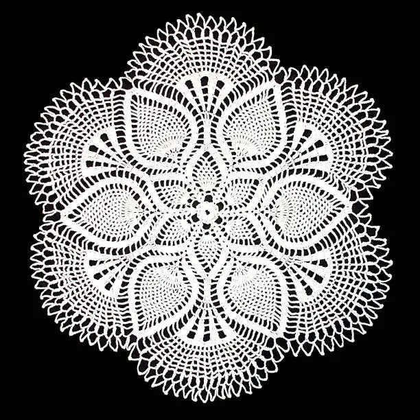 Photo of Isolated crocheted white doily with a pattern of cones on a black background. Round decorative doily.