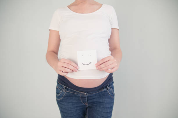 Close-up of pregnant belly with heart eyes emoji isolated on white background as loving mother concept
